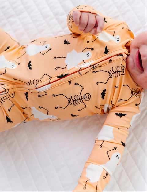Baby wearing an orange Halloween-themed onesie on a white blanket