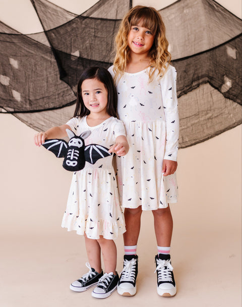 Two young girls in cream colored halloween dresses standing in front of a decorative net.