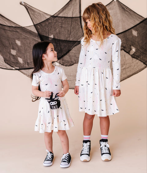Two young girls wearing cream colored Halloween  dresses with black patterns standing in front of a decorative net.
