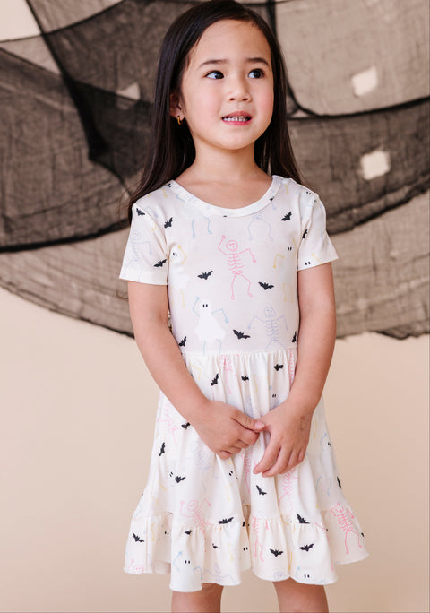 Young girl wearing a white dress with black and pink designs against a neutral background