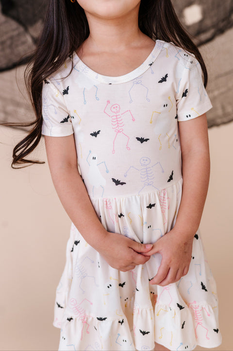 Young girl wearing a white dress with black bat print against a neutral background