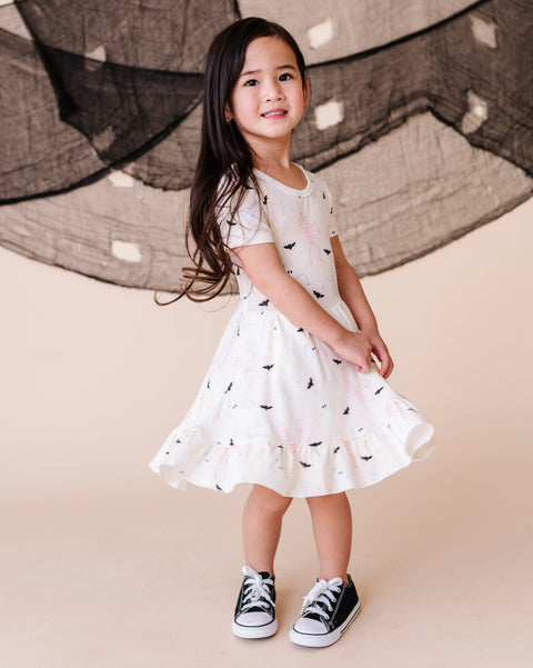 Young girl in a cream dress with halloween patterns standing in front of a large net.