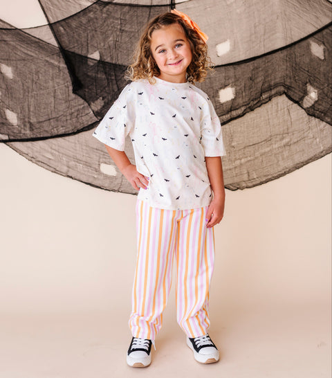 Child wearing a cream colored shirt with halloween patterns and striped pants standing in front of a net