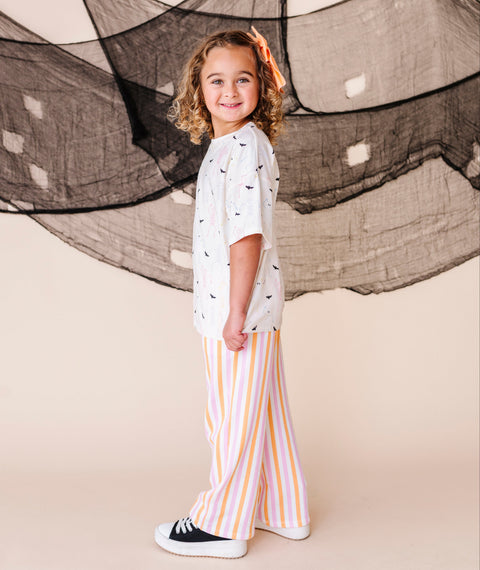 Child wearing a white shirt with black patterns and striped pants standing in front of a large net.