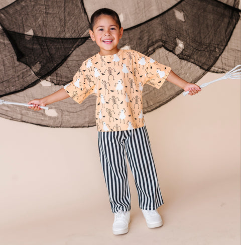 Child wearing a patterned shirt and striped pants standing in front of a netted backdrop.