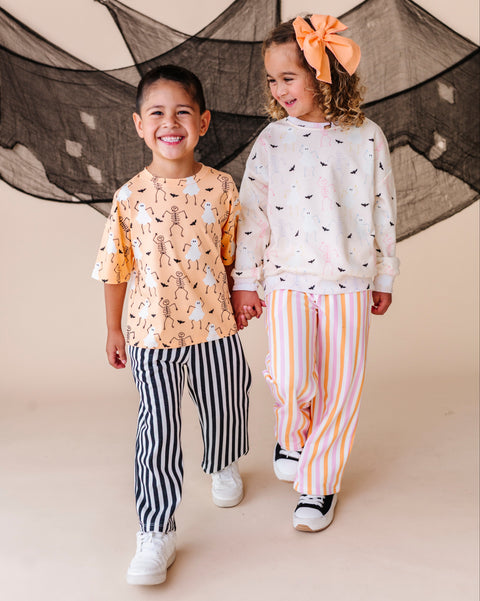 Two children holding hands in front of a decorative net, wearing patterned outfits.