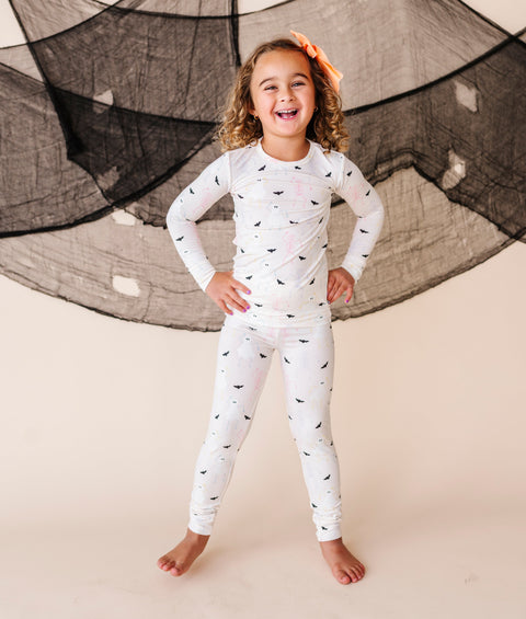 Child wearing a cream pajama set with Halloween patterns against a neutral background