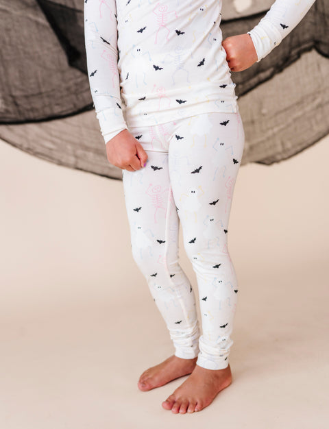 Child wearing a white long-sleeve top and pant pajamas with halloween patterns on a beige surface.
