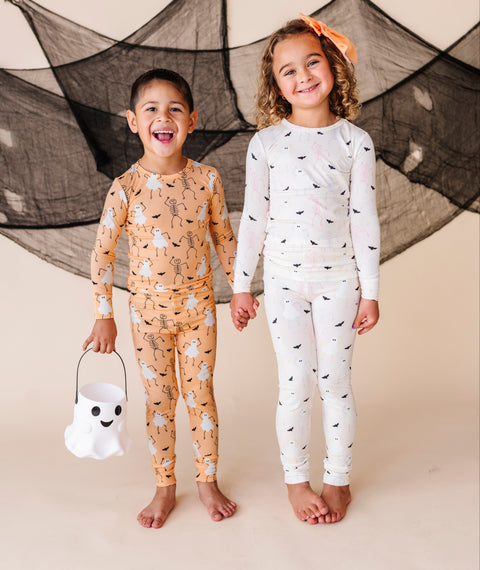 Two children wearing Halloween-themed pajamas standing against a neutral background.