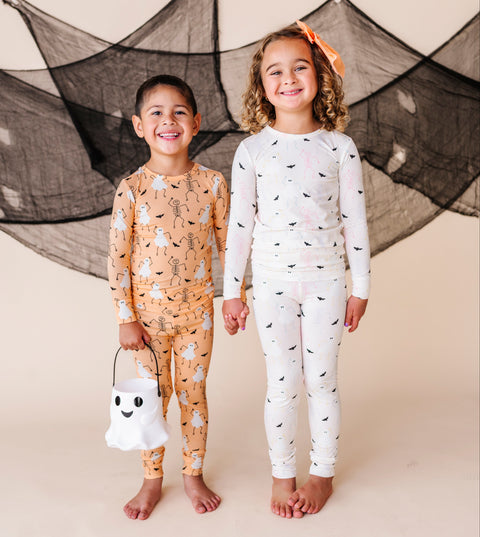 Two children in Halloween-themed pajamas standing in front of a decorative spider web.