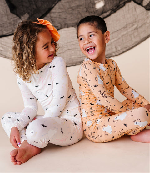Two children in pajamas sitting on a floor, laughing.