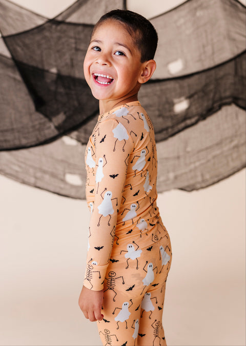 Child wearing a Halloween-themed PAJAMA SET with ghosts and skeletons against a neutral background