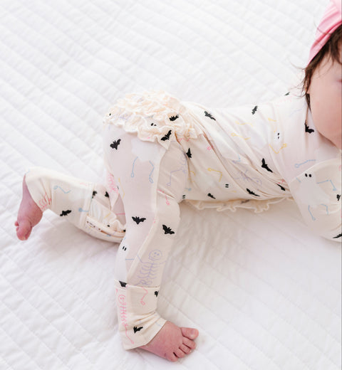 Baby in a cream romper with black bats lying on a white textured surface