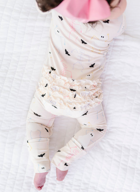 Baby wearing a white onesie with black bats and Halloween icons on a white blanket