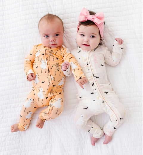 Two babies wearing colorful onesies on a white textured surface