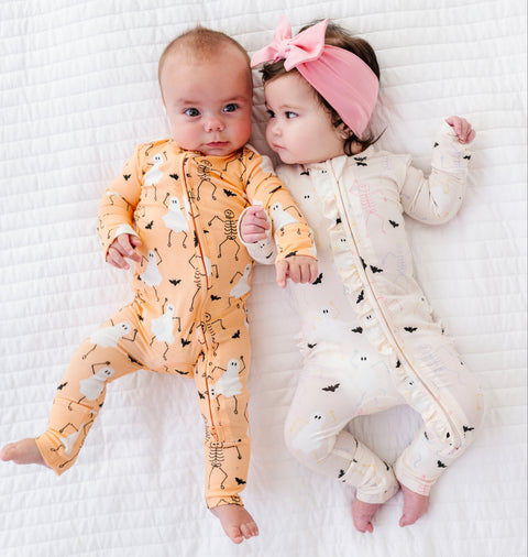 Two babies wearing halloween-themed onesies on a white textured surface