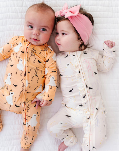 Two babies wearing Halloween-themed onesies on a white blanket.