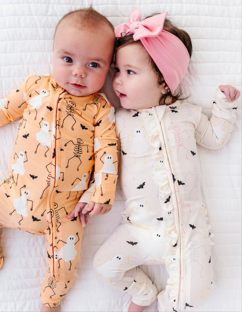 Two babies in Halloween-themed outfits lying on a white textured surface.