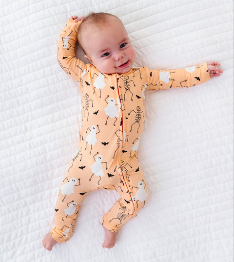 Baby wearing a orange-colored onesie with Halloween-themed design on a white textured surface